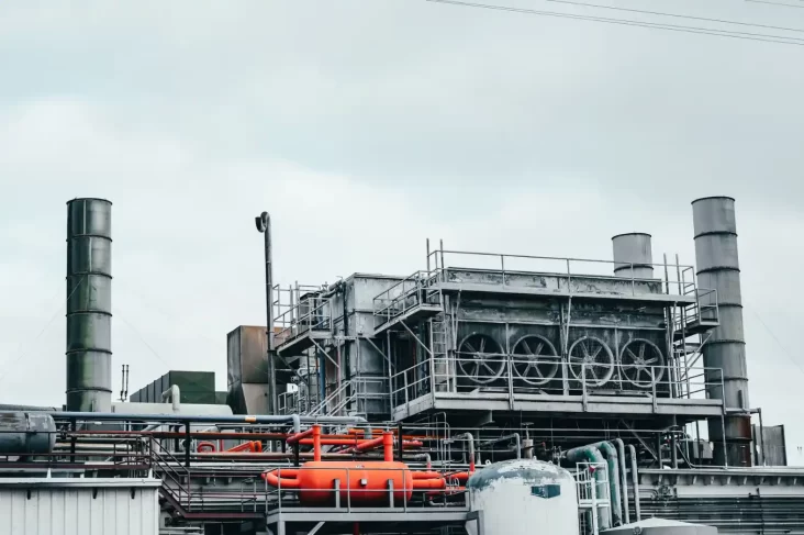 Planta industrial com tubulações, estrutura metálica e grandes dutos de exaustão, cenário para o guia Escolher Manutenção Industrial em Curitiba 2026. Instalação em operação.